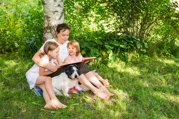 Mother reading a book to daughters in a summer garden setting