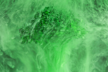 Fresh broccoli in cloud of green color paint in water. Artistic nutrition concept. Science of food action photography. Creative concept of vegetarianism, benefits of vegetables