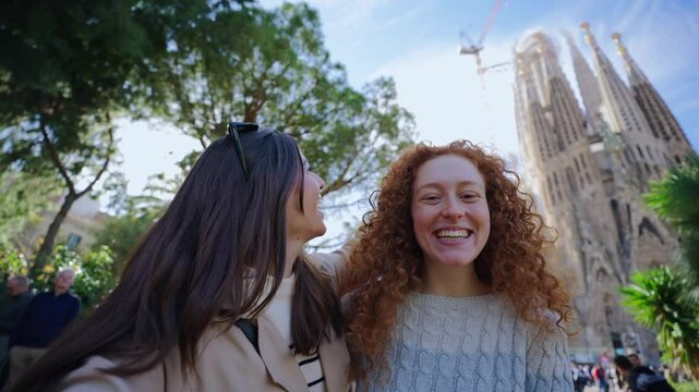 Young funny caucasian women friends taking selfie video call in front of Sagrada Familia in Barcelona. Beautiful girl on street of European city enjoying vacation happy and smiling. Tourist people