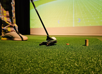 Golfer prepares to putt on artificial turf with virtual course display in background