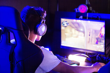 Professional gamer is playing a computer game on PC at cyber club. Player is participating in E-sports competition at gaming cafe. Gamer playing tactical shooter game during cyber sport tournament