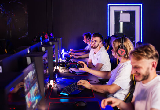 Male players are constantly talking through professional gaming headset. Five guys are using gaming mouse keyboard while playing first-person shooter game. LAN games cyber sport tournament