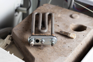 The electric heating element and temperature sensor, thermostat are on the disassembled washing machine. The concept of replacing and repairing spare parts in a washing machine. Scale and hard water