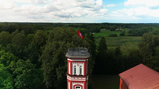 Drone shot over Lithuanian flag on a tower of Alanta Manor in Alanta, Lithuania with dense forest trees and cloudy sky