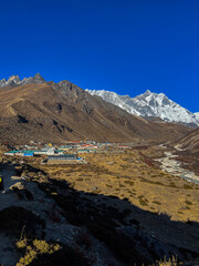 Brown valley with Nepalese village with colorful houses and snowy mountains in the background