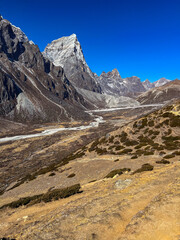 Dry mountain valley with river and high snowy mountains in the background
