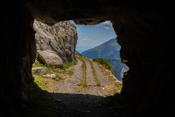 View from inside a tunnel with wagon rails and with mountains in the background
