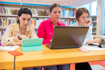Focused women studying with laptops and tablets in library setting