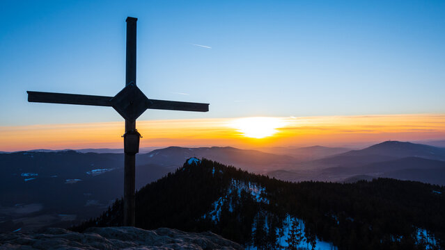 The scenic summit of Grosser Osser with cross on top and breathtaking view to winter mountains during colorful sunset in Bohmerwald nature park, Sumava, Bavaria-Czechia border
