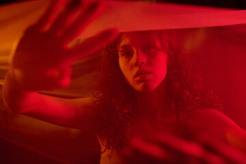 Medium close up of young adult woman gesticulating in air while covered with veil illumed red neon...