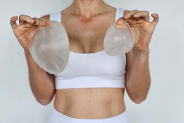 Woman holds silicone breast implants in a neutral setting with casual clothing