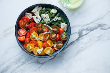 Cherry tomatoes, green beans and blue cheese salad, top view on a white stone background, horizontal shot with space