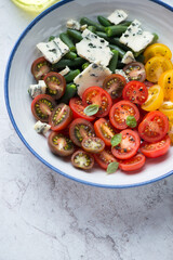 Salad with cherry tomatoes, green beans and blue cheese in a blue and white plate, vertical shot, middle close-up, selective focus