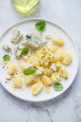 Italian gnocchi served with blue cheese, grated parmesan and basil on a white plate, vertical shot on a white stone surface, high angle view