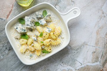 Potato gnocchi with blue cheese in a beige serving tray, horizontal shot on a grey granite background with space, above view