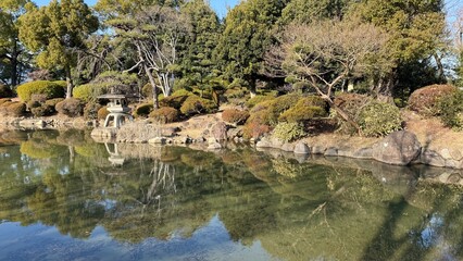 静かな池が周囲の木々や伝統的な石灯籠を映し出す、日本庭園の穏やかな美しさを写した写真です。