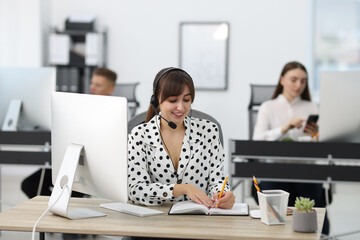 Saleswoman making notes while talking to client via headset at desk in office