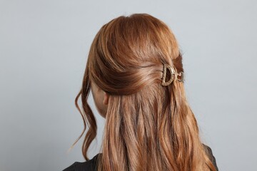 Teenage girl with stylish hair clip on light grey background, back view