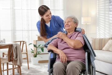 Caregiver covering senior woman with blanket indoors. Home health care service