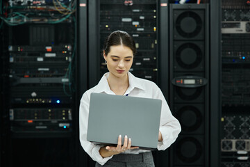 An IT specialist in a white shirt works on a laptop amidst server racks in a data center.