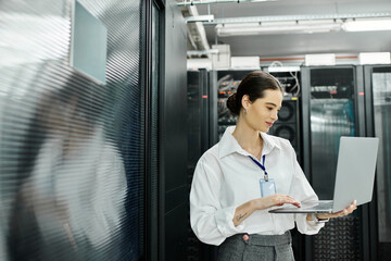 A dedicated woman in a white shirt works diligently on a laptop in a sleek server room environment.
