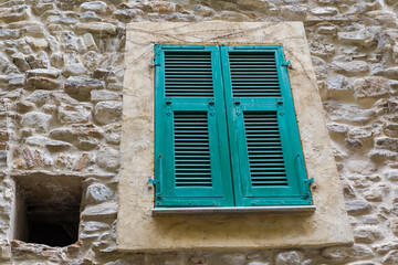 Ancient stone wall with window covered with wooden exterior shutters