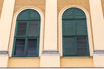 Arched windows with closed green wooden shutters in yellow wall