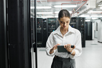 A focused woman works on her tablet in a sleek server room, ensuring smooth operations.