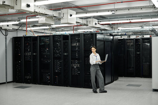 In a modern server room, a woman in a white shirt manages computer systems with focus and skill. - Powered by Adobe