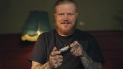 Excited gamer playing video game, portrait of man with joystick at home. Handsome bearded male person have fun and joy, computer game addiction and entertainment, hipster with tattoo and piercing