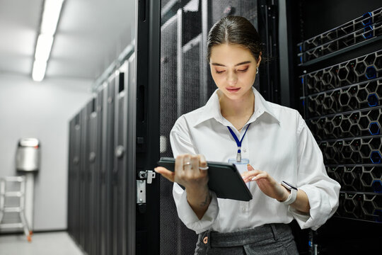 A woman in a white shirt supervises server operations using a tablet in a data center. - Powered by Adobe