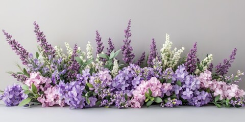Lavender and purple artificial flowers arrangement with green leaves on a soft gray background for spring decor in a horizontal composition
