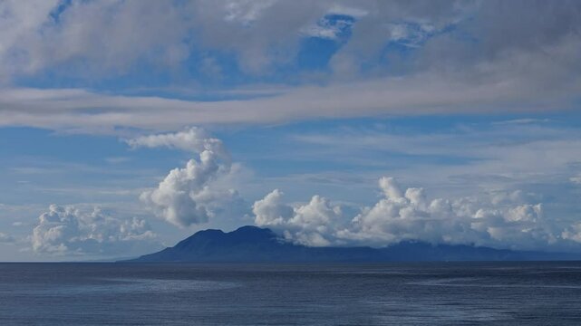 A breathtaking view across the Surigao Strait in the Philippines, showcasing calm blue waters and the distant islands of Leyte and Panaon silhouetted against a cloudy horizon.