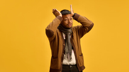 A man in brown cardigan and scarf suffering from headache, painful migraine on a yellow studio...