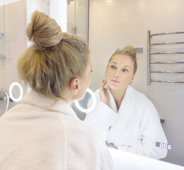 woman looking in the mirror in the bathroom and taking care of her skin.