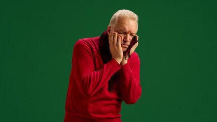 Elderly man in scarf and red sweater suffering from intense toothache and inflammation symptoms on...