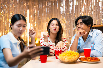 Selfies on friends night out. Three happy friends taking a selfie while having dinner and drinks at a house party. Group of cheerful asian friends having fun together on the weekend.