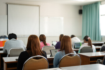 Fototapeta premium Students engage in a lecture, sitting at desks with their attention focused on the lecturer at the front of the classroom. The lecturer uses a projector screen for the presentation.