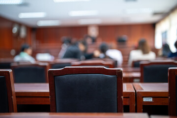 A classroom with a black chair in the foreground. The chair is empty and the room is filled with...