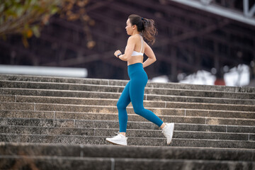 Obraz premium A woman is running up a set of stairs. She is wearing a white tank top and blue pants