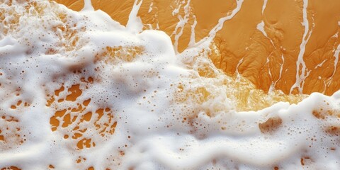 Closeup of golden orange sand with white foamy waves creating intricate textures and patterns along...