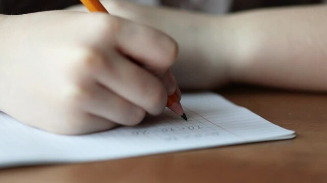 a child writes with a pencil and solves math examples in a checkered notebook. primary school education