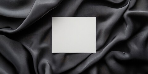 Blank square invitation card on dark gray satin fabric, centered horizontally, smooth drapery creating elegant contrast for design purposes.