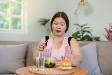 Determined overweight woman rejecting a burger, choosing a fresh salad instead on her weight loss...