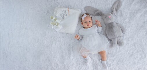 The baby is dressed in a white dress and lies with a bunny, a chain with a cross. Baptism of a child