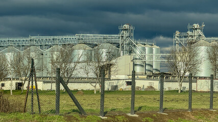 Industrial grain silos under a stormy sky highlight agricultural production and storage challenges...