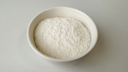 A bowl of shredded coconut on a white background, ideal for baking concepts and tropical-themed holiday recipes