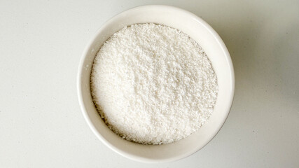 A bowl of white shredded coconut sits on a table, perfect for holiday baking and dessert preparation