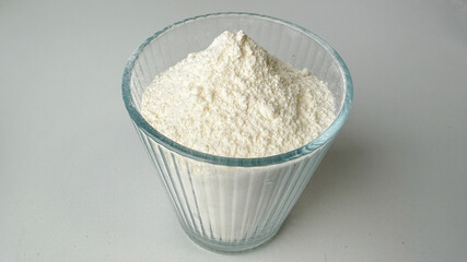 A clear glass filled with baking flour sits on a neutral surface, symbolizing culinary preparation and holiday baking essentials