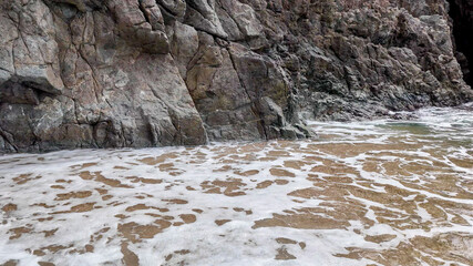 Foamy ocean waves gently lap against rugged rocky cliffs, symbolizing the power of nature and coastal erosion issues